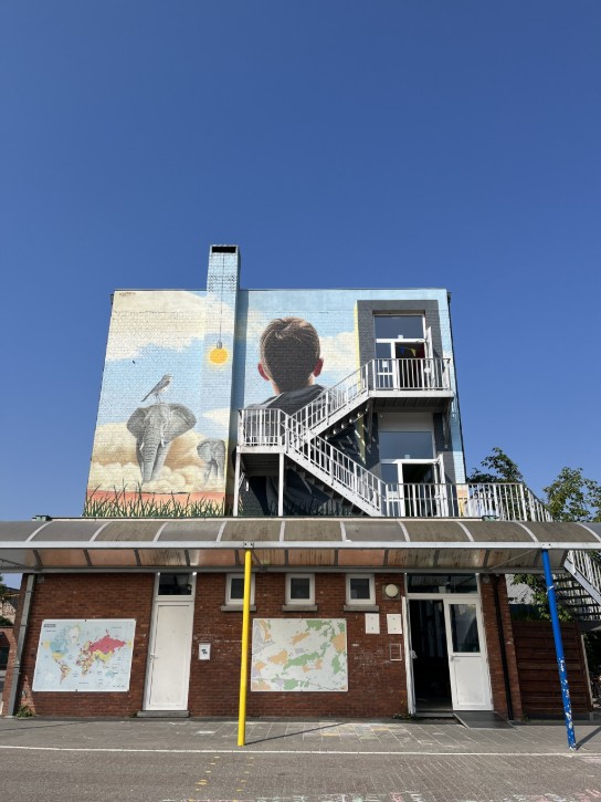 Muurschildering op school De Regenboog met jongen, olifanten en vogel, trappen en blauwe lucht. (vergroot foto)