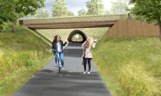 Twee vrouwen groeten elkaar op een fietspad onder een brug, omgeven door groen en bomen. (vergroot foto)