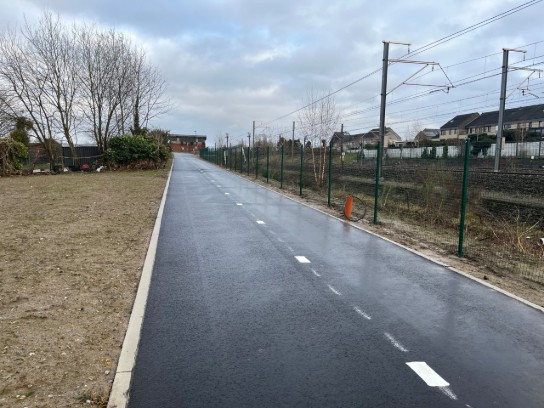 Natte, lege weg naast spoorlijn met hekken en huizen onder bewolkte lucht. (vergroot foto)