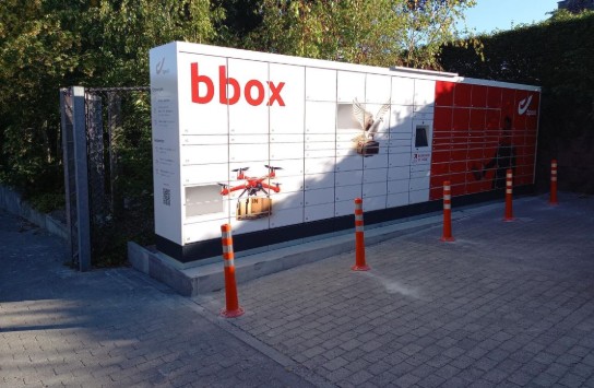 Bbox pakketkluizen buiten, omgeven door oranje paaltjes en groen struikgewas. (vergroot foto)