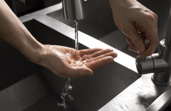 Hand die water opvangt uit een kraan boven een spoelbak, met een hand die de kraan bedient. (vergroot foto)