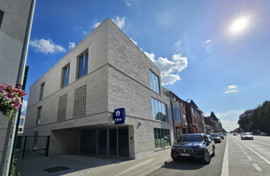 Modern politiebureau in een lichte bakstenen gebouw aan een zonnige straat met geparkeerde auto's. (vergroot foto)