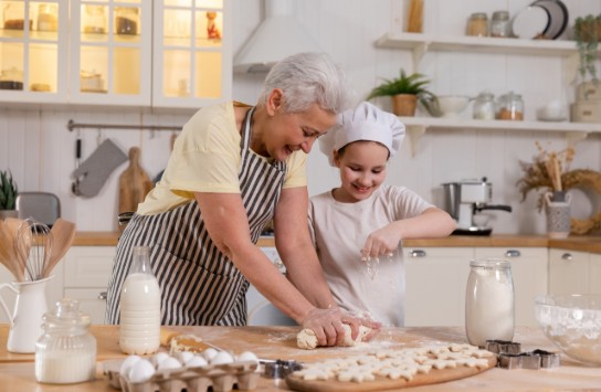 Oma en kleindochter bakken samen koekjes in een gezellige, lichte keuken. (vergroot foto)