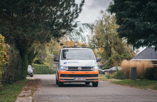 Witte en oranje politiebus rijdt op een rustige straat omringd door bomen en huizen. (vergroot foto)