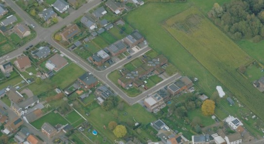 Luchtfoto van een woonwijk met huizen, tuinen en een groot groen veld aan de rechterkant. (vergroot foto)