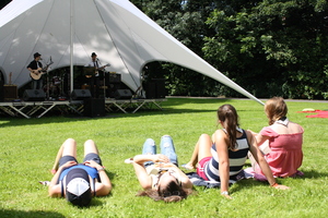 Een groepje mensen kijkt en luistert naar de artiesten die muziek spelen op een podium in het park van de oude abdij