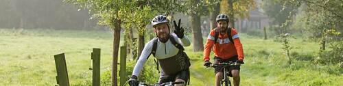 twee mountainbikers op een fiets door het veld